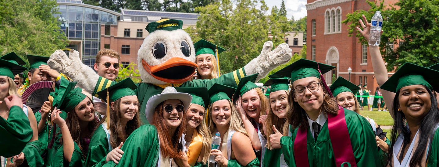 A crowd of graduates in green gowns and caps pose with the Duck